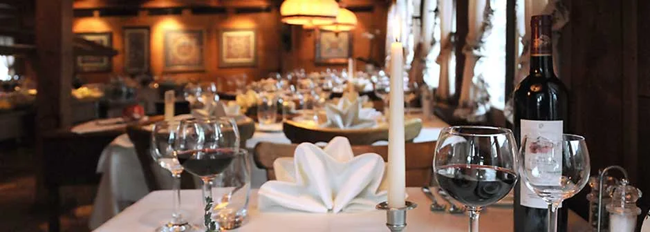 Candlelit restaurant table with red wine glasses, a wine bottle, and folded white napkins.
