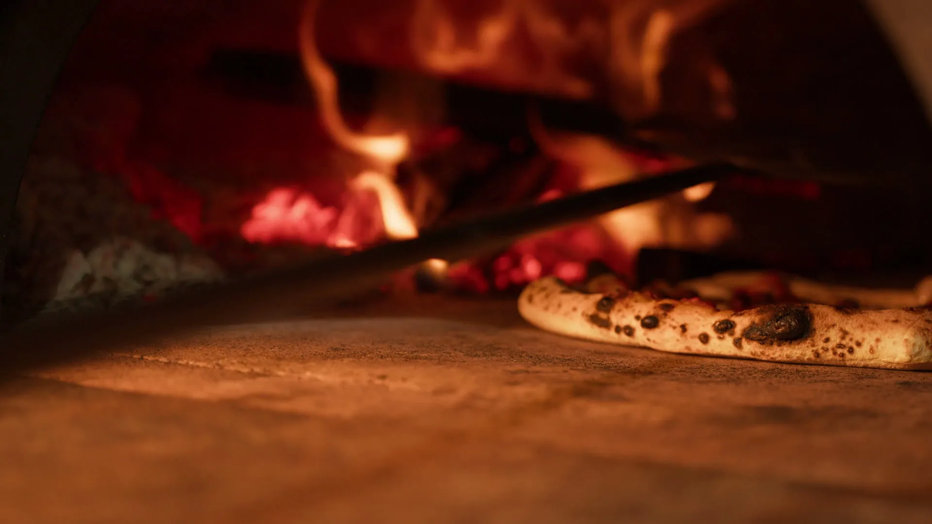 A Neapolitan pizza baking directly on the stone floor of a roaring wood-fired oven.