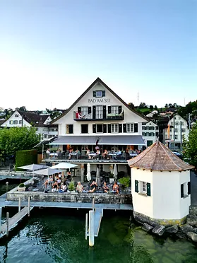 Aerial view of Bad am See building rising dramatically over Lake Zurich waters, perfectly capturing the historic lakeside restaurant's stunning setting.