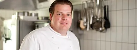 Chef in white kitchen uniform stands confidently in a professional kitchen.