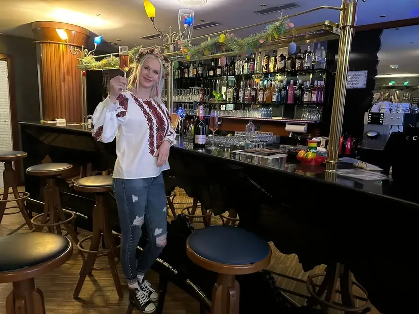 Blonde owner raises a champagne flute behind the well-stocked bar of Madame Figaro.