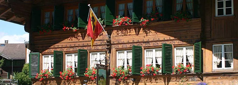 Traditional Swiss chalet exterior with green shutters, red geraniums, and a cantonal flag.
