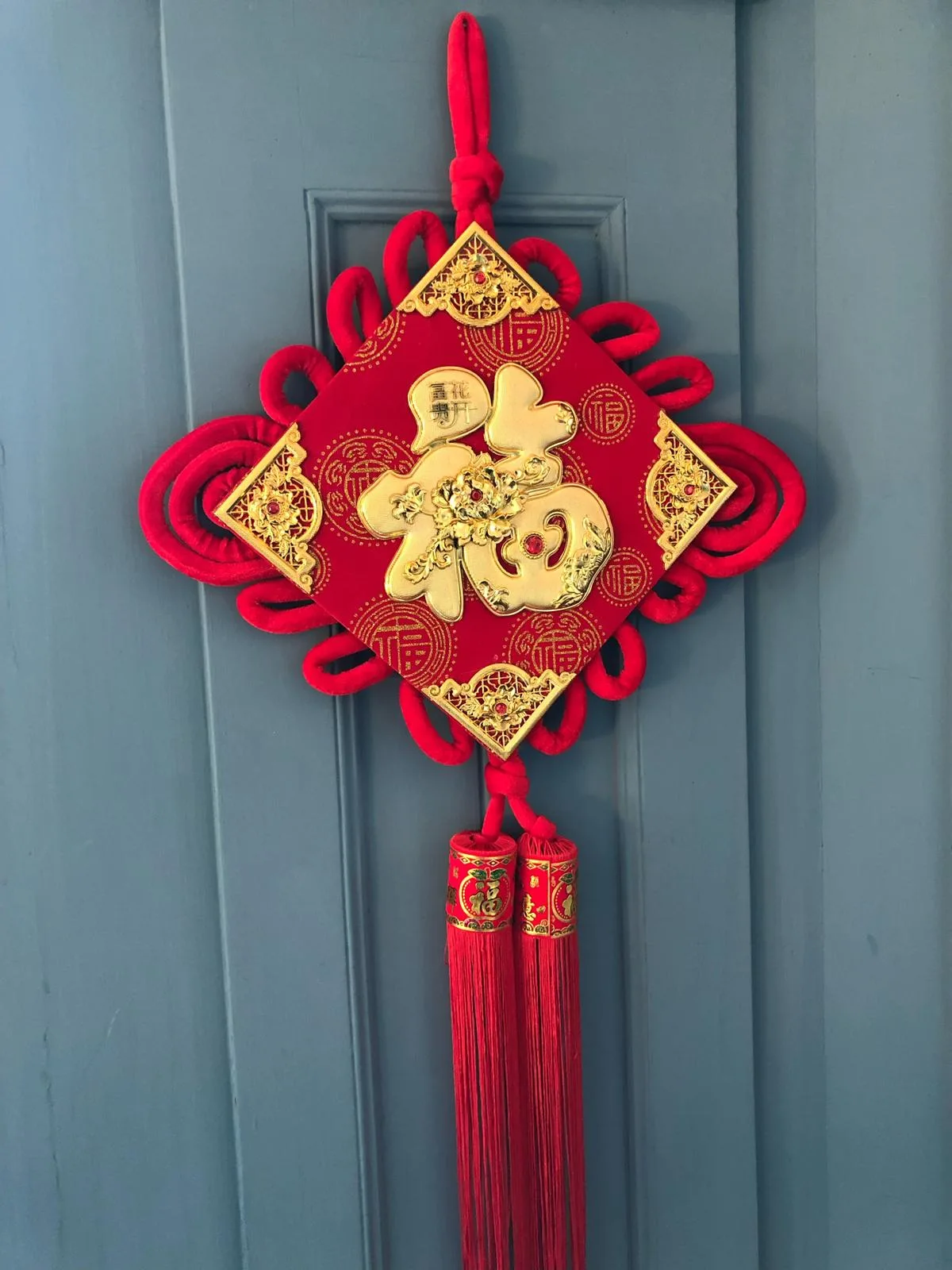 Traditional red Chinese Fu knot decoration hanging on a grey door.