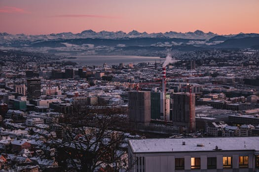 Elegante Rooftop-Bar mit Panoramablick über eine Schweizer Stadt bei Sonnenuntergang, wo Gäste an modernen Tischen sitzen und Cocktails genießen.