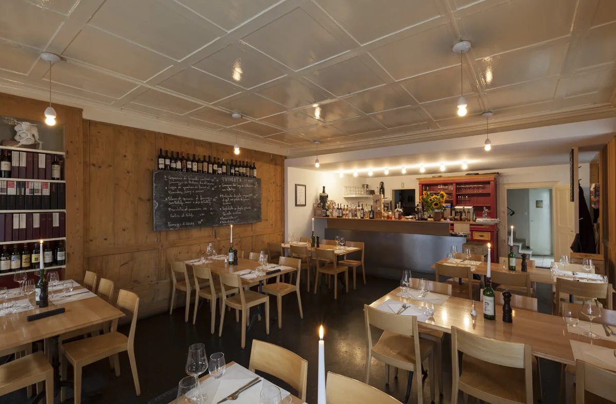 Sunny outdoor terrace of the Vinothek Freischütz in a charming European old-town square with guests dining.