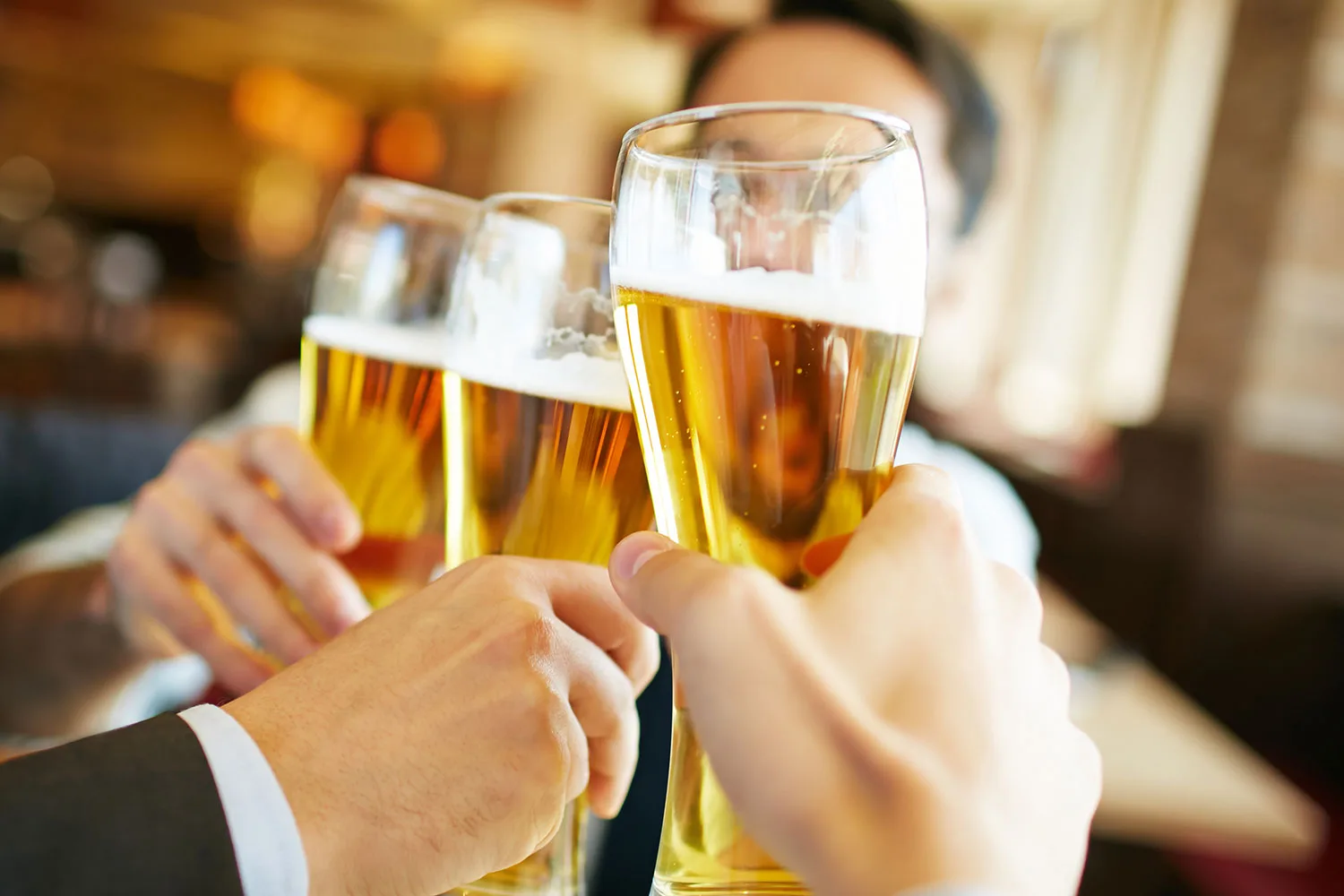 Three glasses of beer clinking together in a warm, convivial restaurant setting.