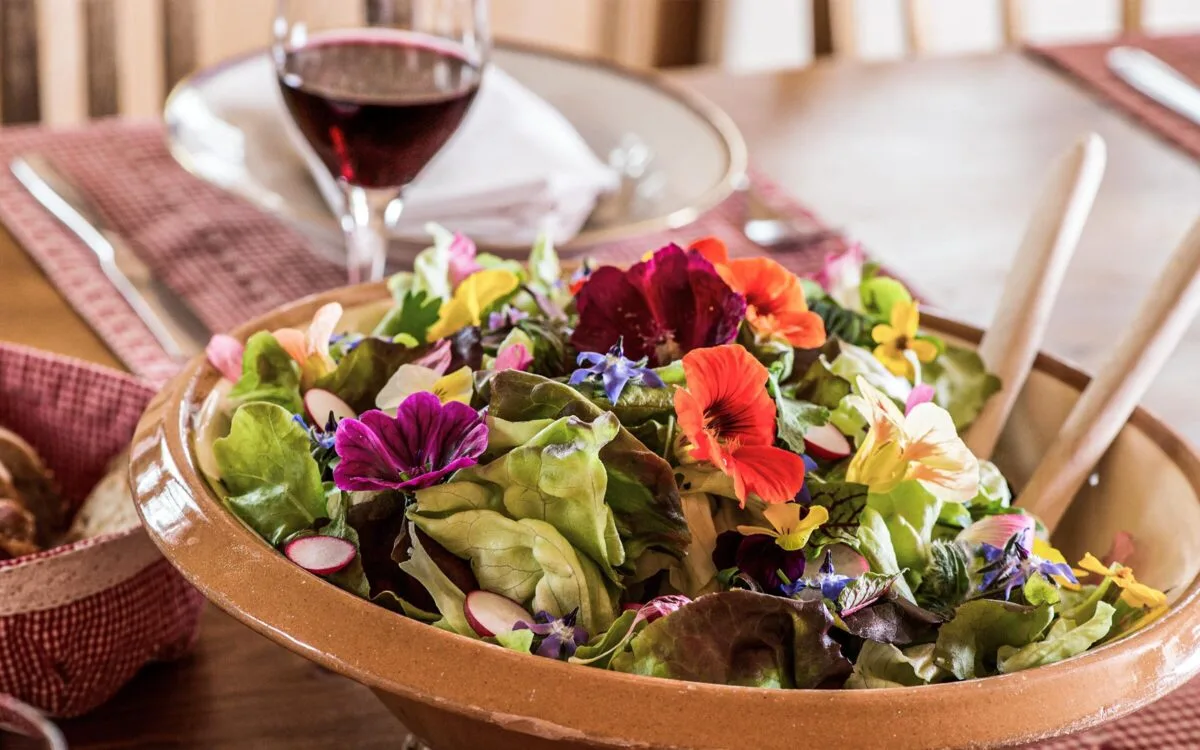 Colourful garden salad decorated with edible flowers served in a traditional earthenware bowl.