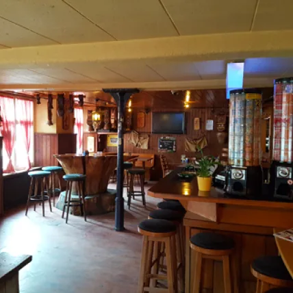 Cozy rustic bar interior with wooden paneling, bar stools, and a television on the wall.
