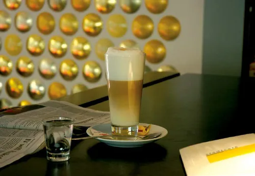 A second latte macchiato shot with softer ambient lighting and a book nearby.