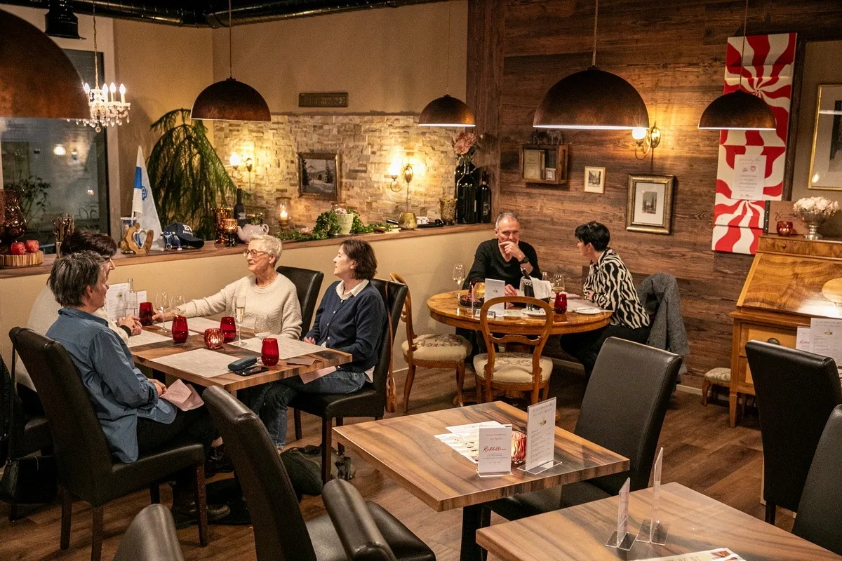 Warm dining room with guests seated at elegantly set tables under copper pendant lights.