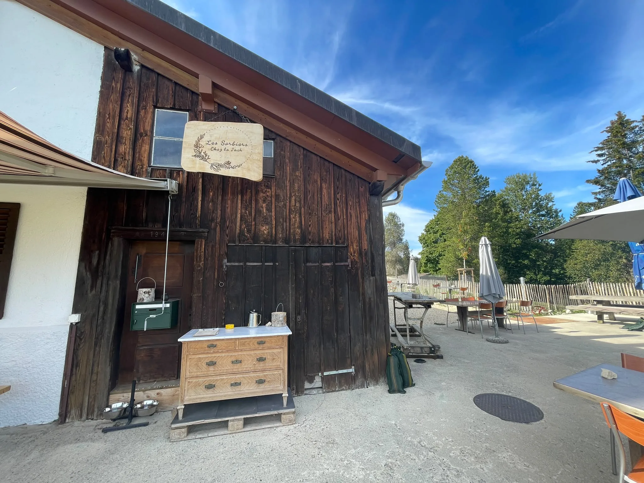 Rustic barn entrance of Chez la Jack with a handcrafted wooden sign and outdoor service dresser.