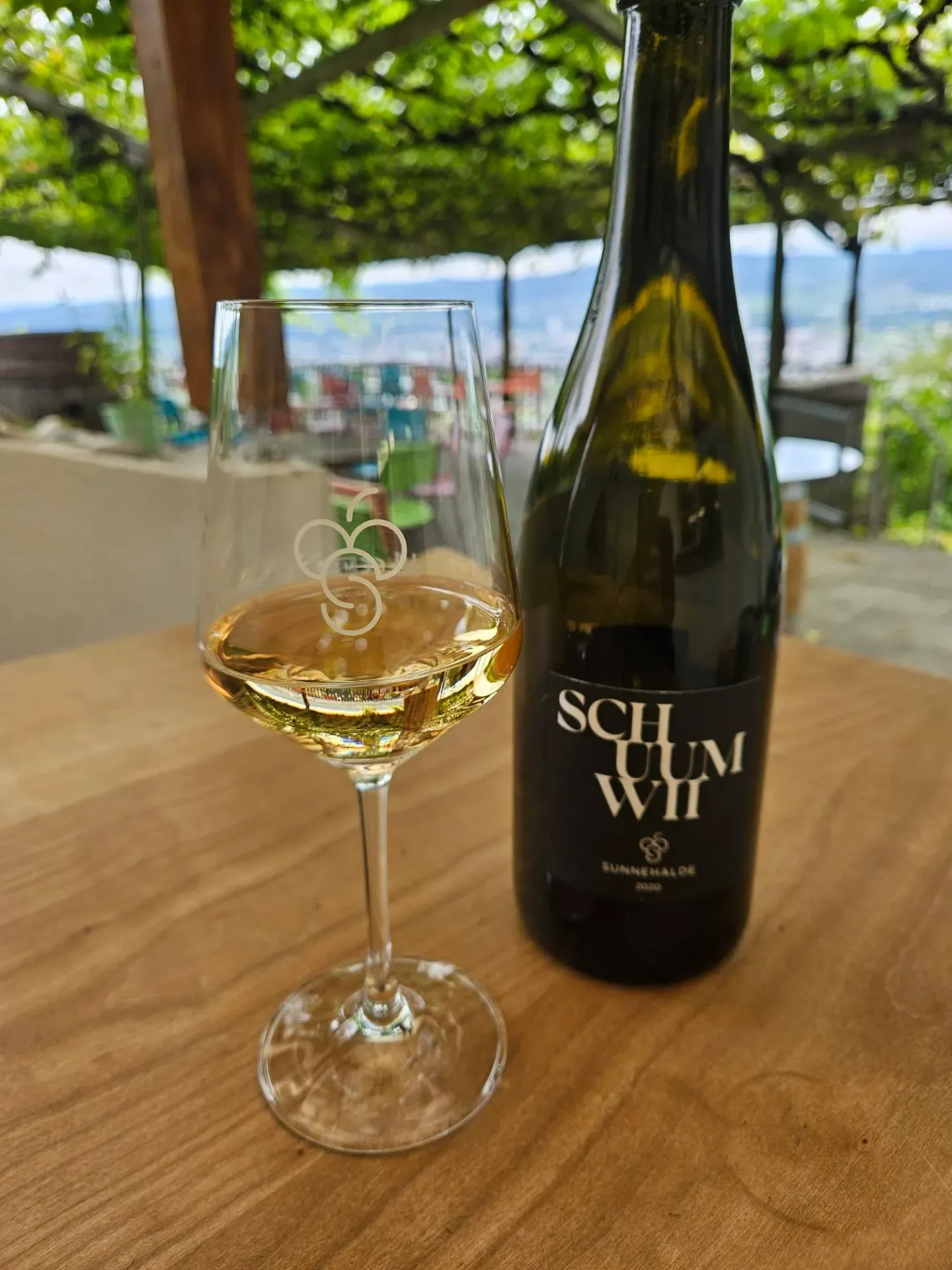 A glass of golden Schuumwii sparkling wine beside its bottle on a sunny vineyard terrace.