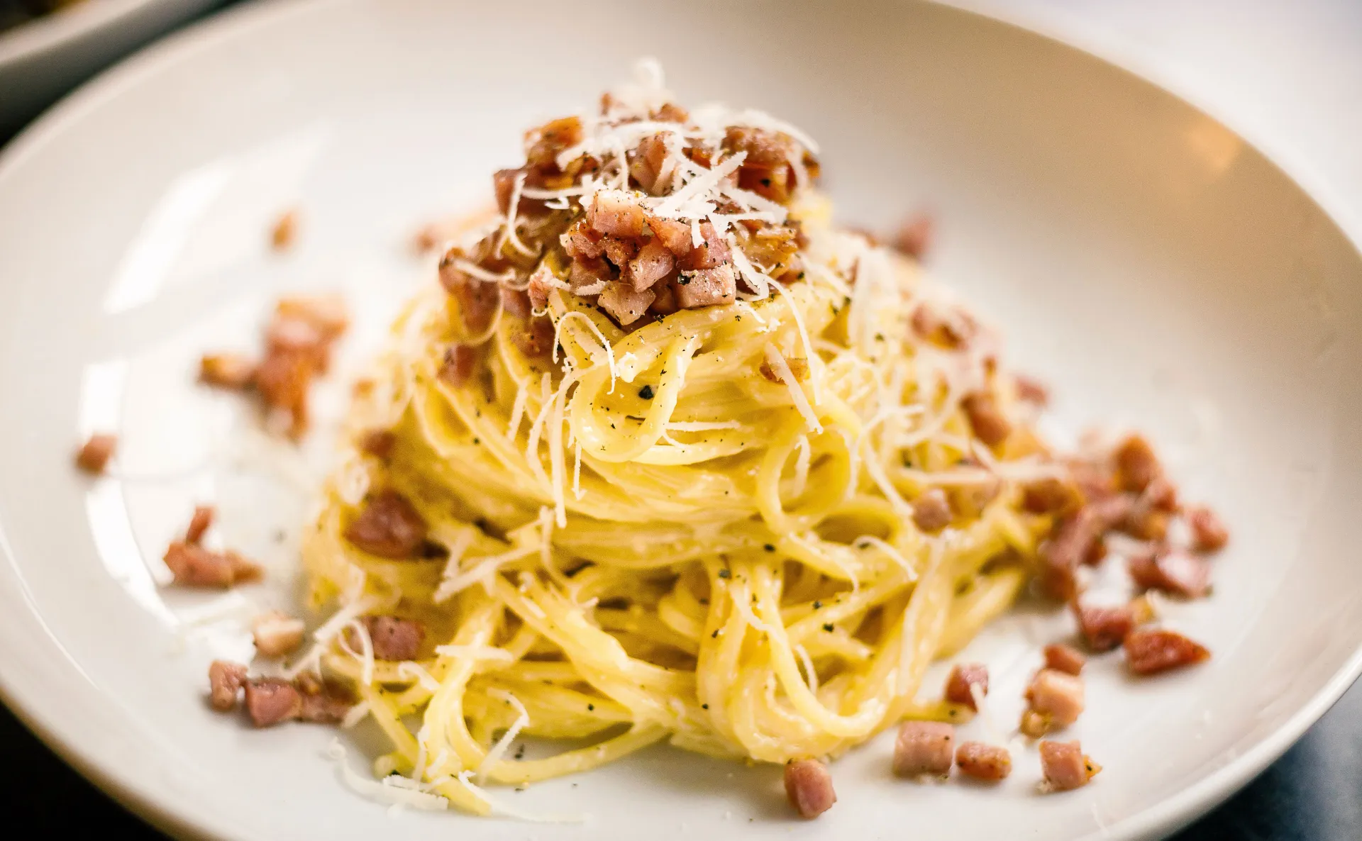 A beautifully plated spaghetti carbonara topped with guanciale and shaved Pecorino cheese.