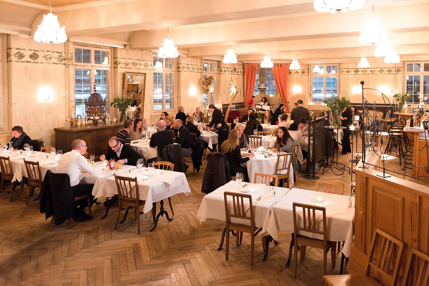 Intimate dinner service in the ornate main salon featuring decorative wall patterns, hanging lamps, and refined table settings embodying Belle Époque atmosphere.