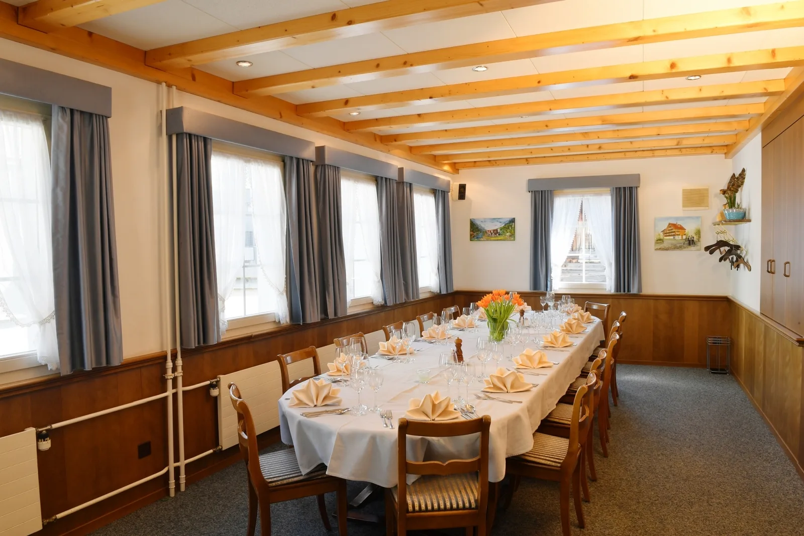 A spacious, traditionally furnished dining hall with exposed wooden ceiling beams and ample natural light, conveying the cozy, timeless ambiance of the Adler.