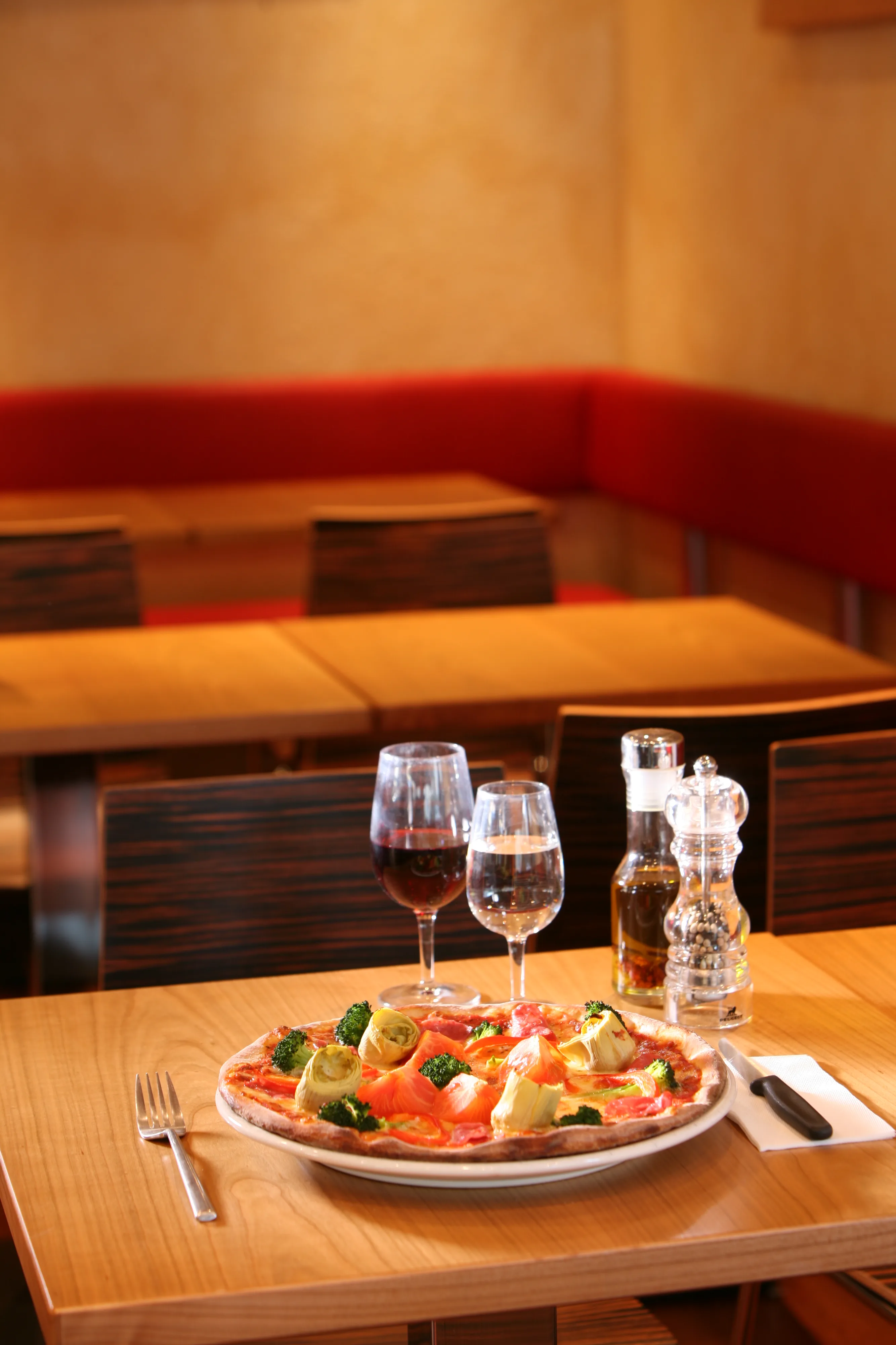 Wood-fired pizza topped with salmon, artichoke hearts, and broccoli served alongside red wine glasses.