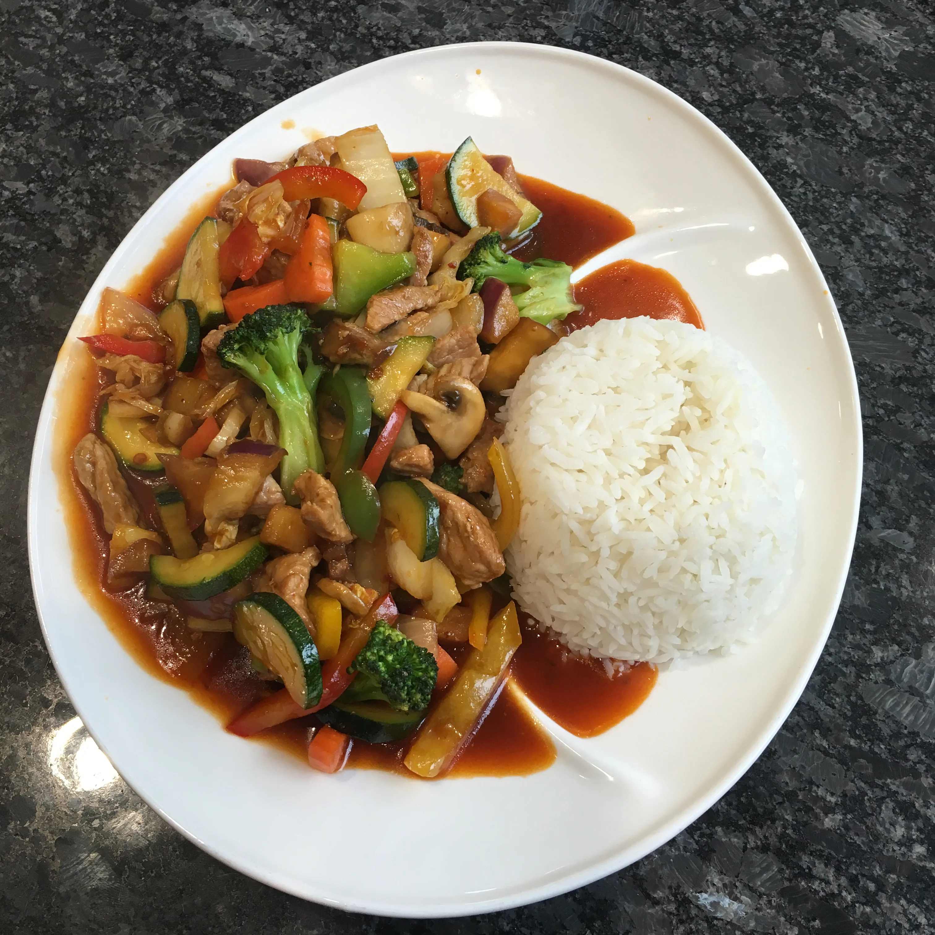 Vibrant stir-fry with chicken, broccoli, zucchini, and peppers in red sauce served with steamed rice.