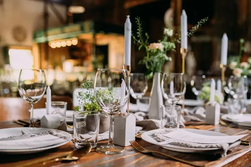 Beautifully set dinner table with candles, wine glasses, white plates, and floral centerpieces in a warm restaurant.