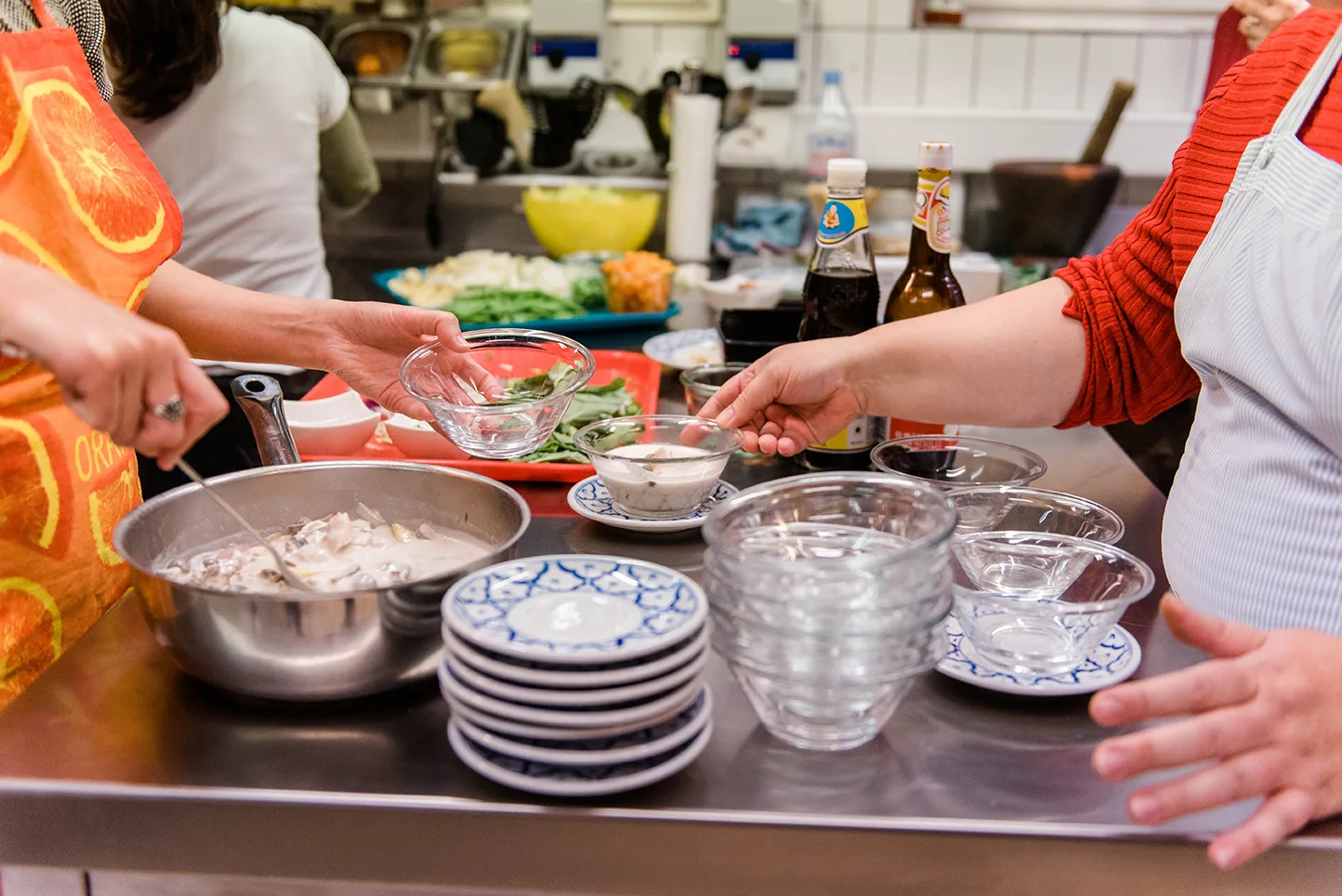 High-resolution view of a Thai cooking class with sauces, plates, and fresh ingredients on the counter.