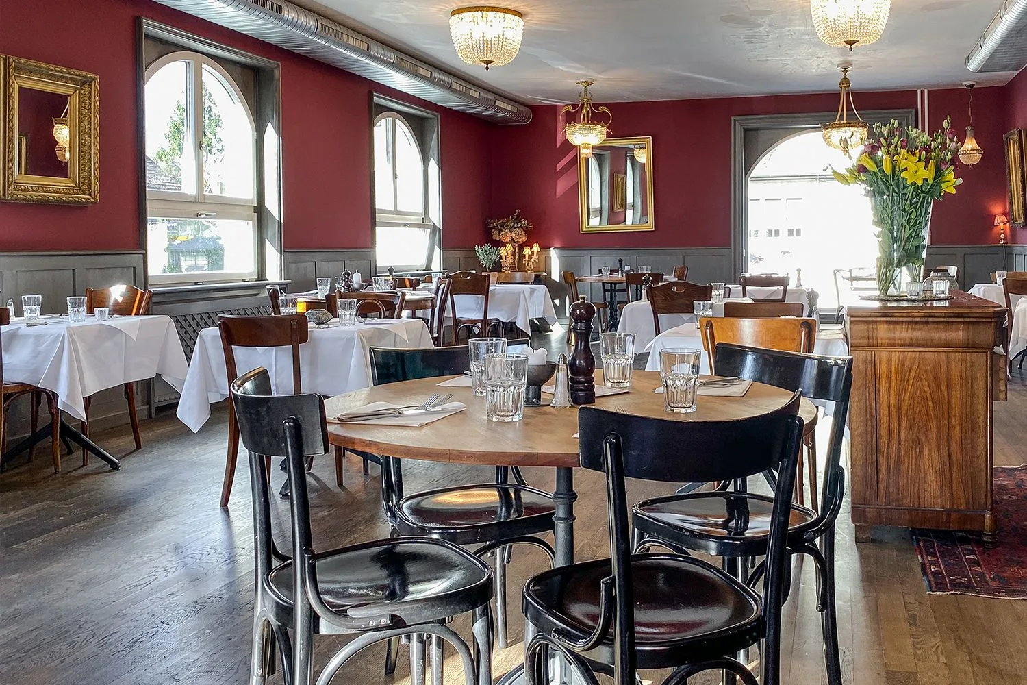Contemporary dining space with bold red walls, elegant table settings, and large windows creating a sophisticated yet welcoming culinary atmosphere.