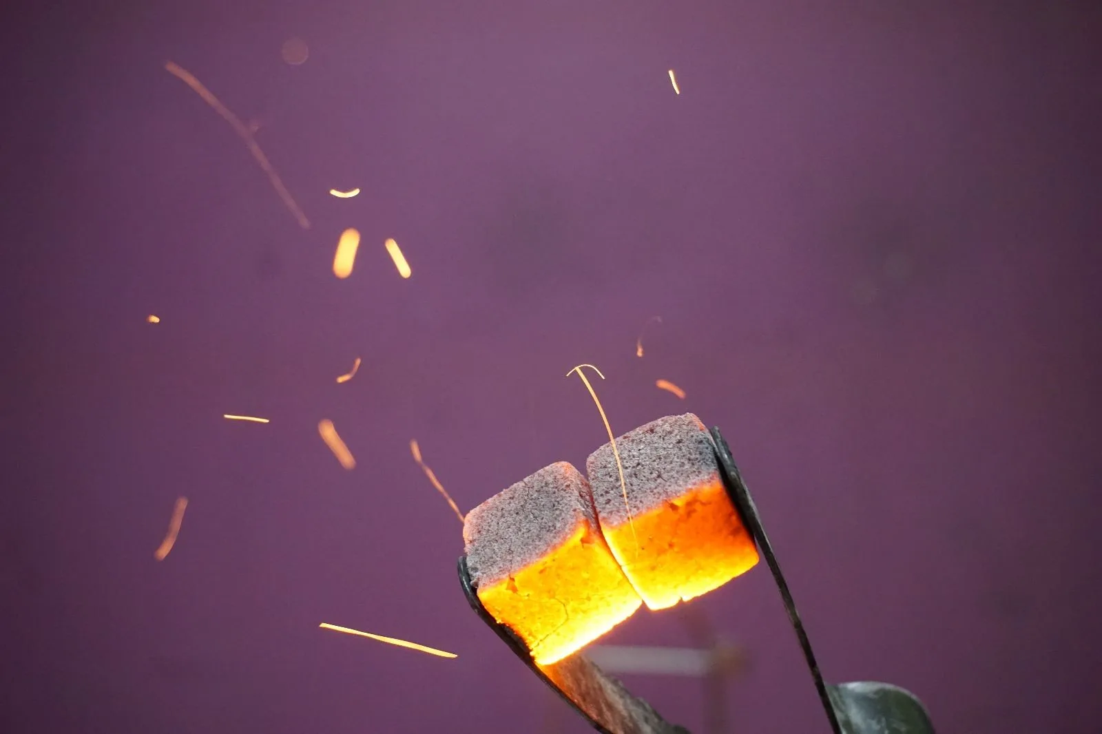 Close-up of intensely glowing red-hot shisha charcoal cube resting in a bowl, radiating orange light.