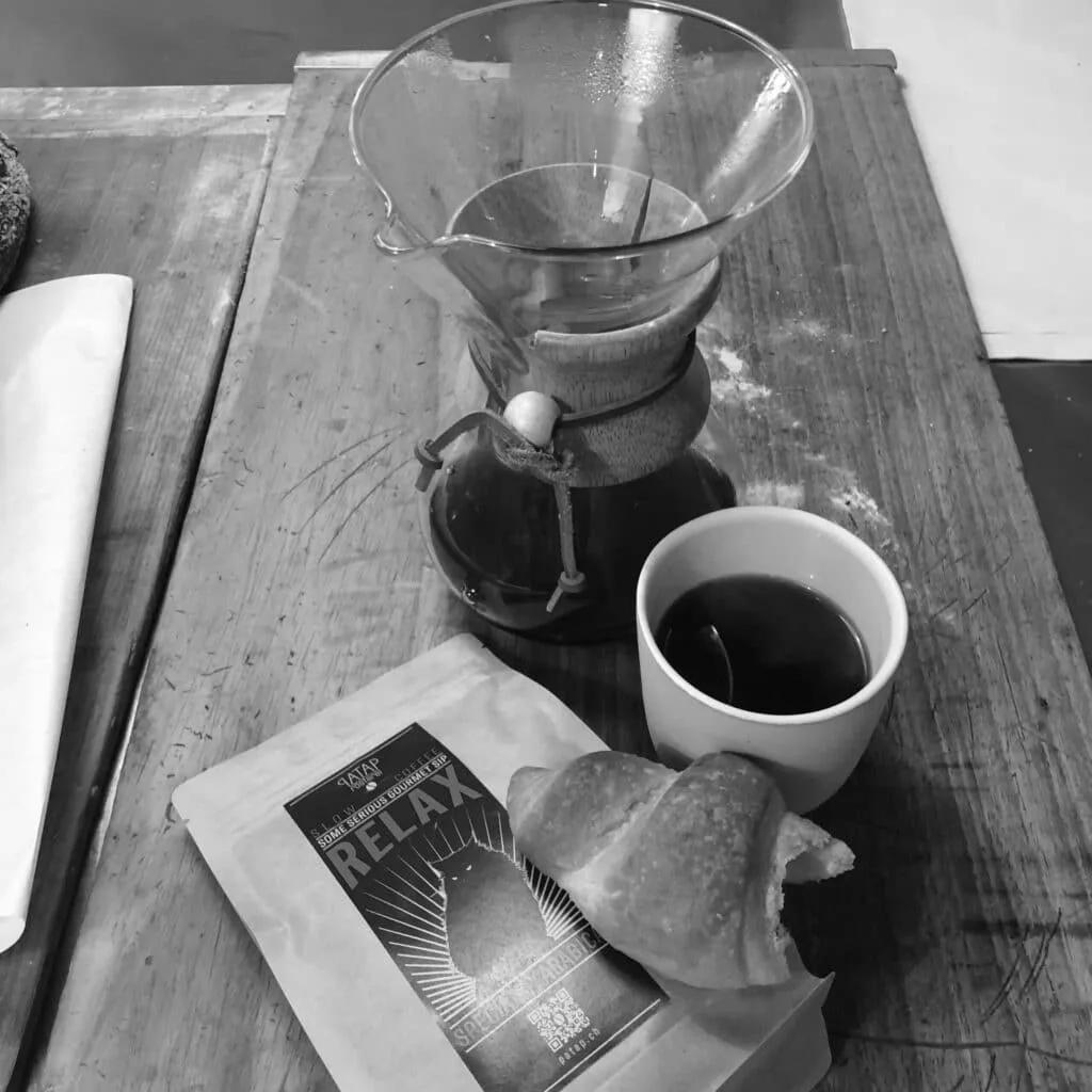 Cosy PATAP café interior viewed through a pass-through window with baked goods under glass domes.